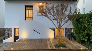 Une maison moderne à deux étages, avec un toit en tuiles, une terrasse en bois et un petit arbre dans le jardin.