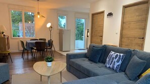 Un salon moderne avec un canapé gris, une petite table ronde agrémentée d’une plante, et un coin repas comprenant une table et des chaises.