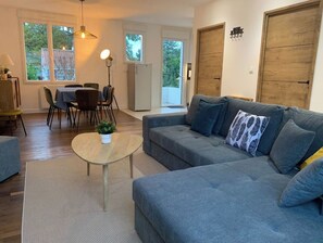 Un salon moderne avec un canapé gris, une petite table ronde agrémentée d’une plante, et un coin repas comprenant une table et des chaises.