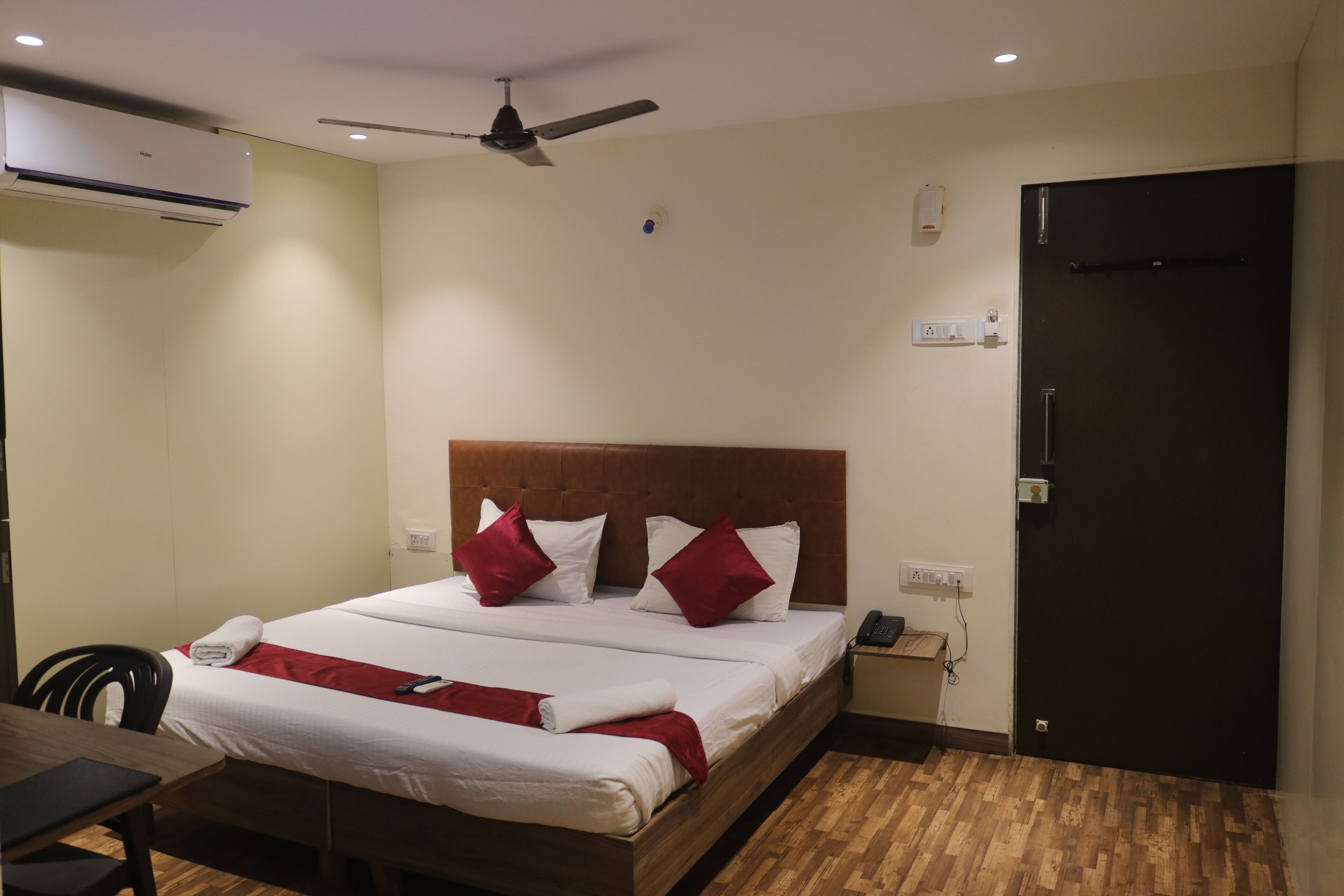 A hotel room with a bed, a desk, a chair, a ceiling fan, and a door.