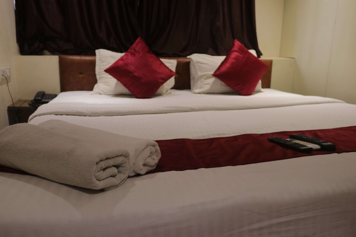 A neatly made bed with a red and white bedspread, two red pillows, and a rolled white towel.