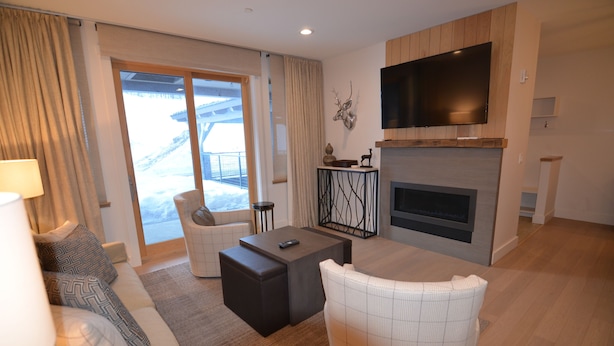 A modern living room with a sofa, armchair, coffee table, fireplace, and a TV mounted on the wall.