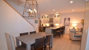 A modern kitchen with white cabinets, a stainless steel refrigerator, and a dining area with a wooden table and chairs.