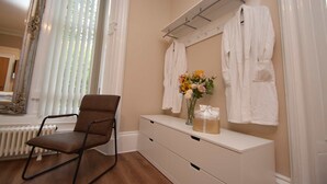 A bathroom with a wooden floor, a white vanity with a mirror, a towel rack, and a chair. - Rosedene Highland House - Emperor Apartment 1 (Inverness)