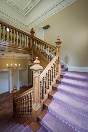 A grand staircase with ornate wooden balusters and a purple carpeted landing.