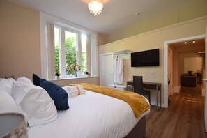 A bedroom with a large bed, a desk, a TV, and a bathroom visible through an open door.