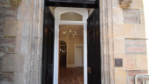 A hallway with a black door, a chandelier, and a patterned floor. - Rosedene Highland House - Emperor Apartment 2 (Inverness)