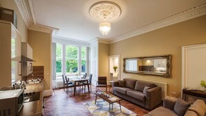 A spacious living area with a dining table, sofa, and a large mirror. - Rosedene Highland House - Emperor Apartment 2 (Inverness)