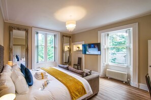 A spacious bedroom with a large bed, a television, and a view of the outdoors through the windows.