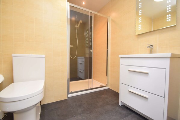 A bathroom with a toilet, a shower enclosure, and a vanity with drawers.