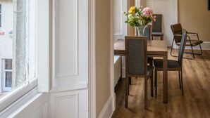 A hallway with a radiator, a dining area with a table and chairs, and a window with a view of the outside. - Rosedene Highland House - Emperor Apartment 6 (Inverness)