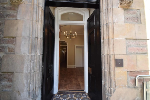 A hallway with a black door, a chandelier, and a patterned floor.