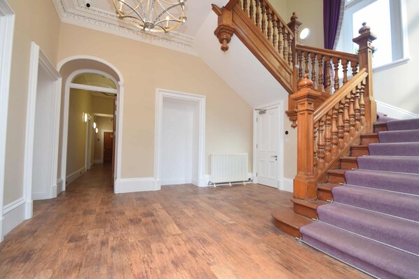 A spacious hallway with wooden flooring, a wooden staircase with purple carpeted steps, and a white radiator. - Rosedene Highland House - The Cottage Apartment 8 (Inverness)