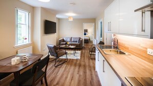 A modern kitchen with a wooden countertop, a sink, and a dining area with a table and chairs. - Rosedene Highland House - The Cottage Apartment 10 (Inverness)