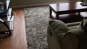 Una sala de estar con un gran ventanal, un ventilador de techo, una mesa de centro de madera y un sofá color beige.