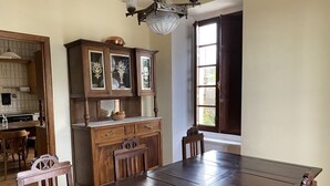 Un comedor con mesa y sillas de madera, una vitrina y una ventana con vistas a la vegetación.