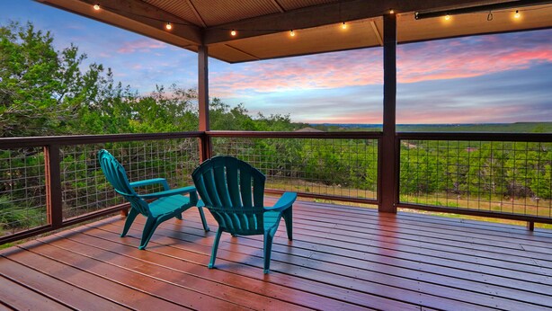 A covered outdoor deck with two chairs and a table, overlooking a scenic landscape with trees and a colorful sky. - Canyon Breeze I 3 Bedroom I Pet Friendly I Canyon Lake! (Canyon Lake)