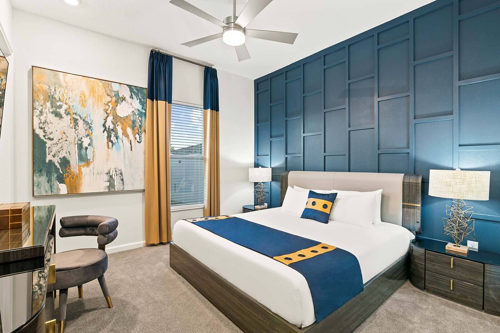 Habitación de hotel con una cama grande, un escritorio con silla, un ventilador de techo y un cuadro abstracto de grandes dimensiones en la pared.