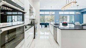 A modern kitchen with a central island, stainless steel appliances, and a view to the outdoor dining area. - Fun Home w/ Trampoline RM, Pirate Theme BR, Arcade, Theater & Gym - Near Disney (Davenport)