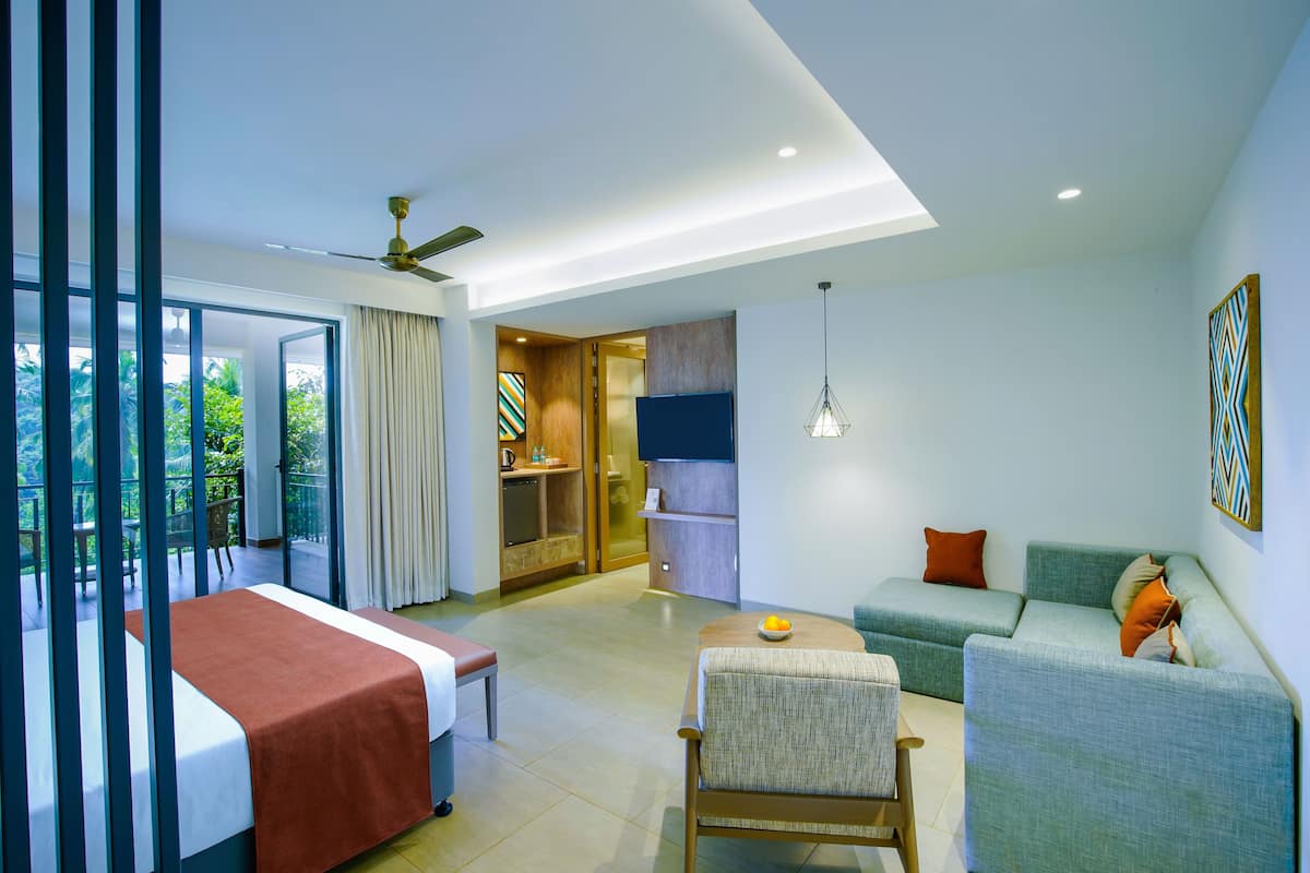 A modern hotel room with a bed, a sofa, a chair, a dining table, and a kitchen area.