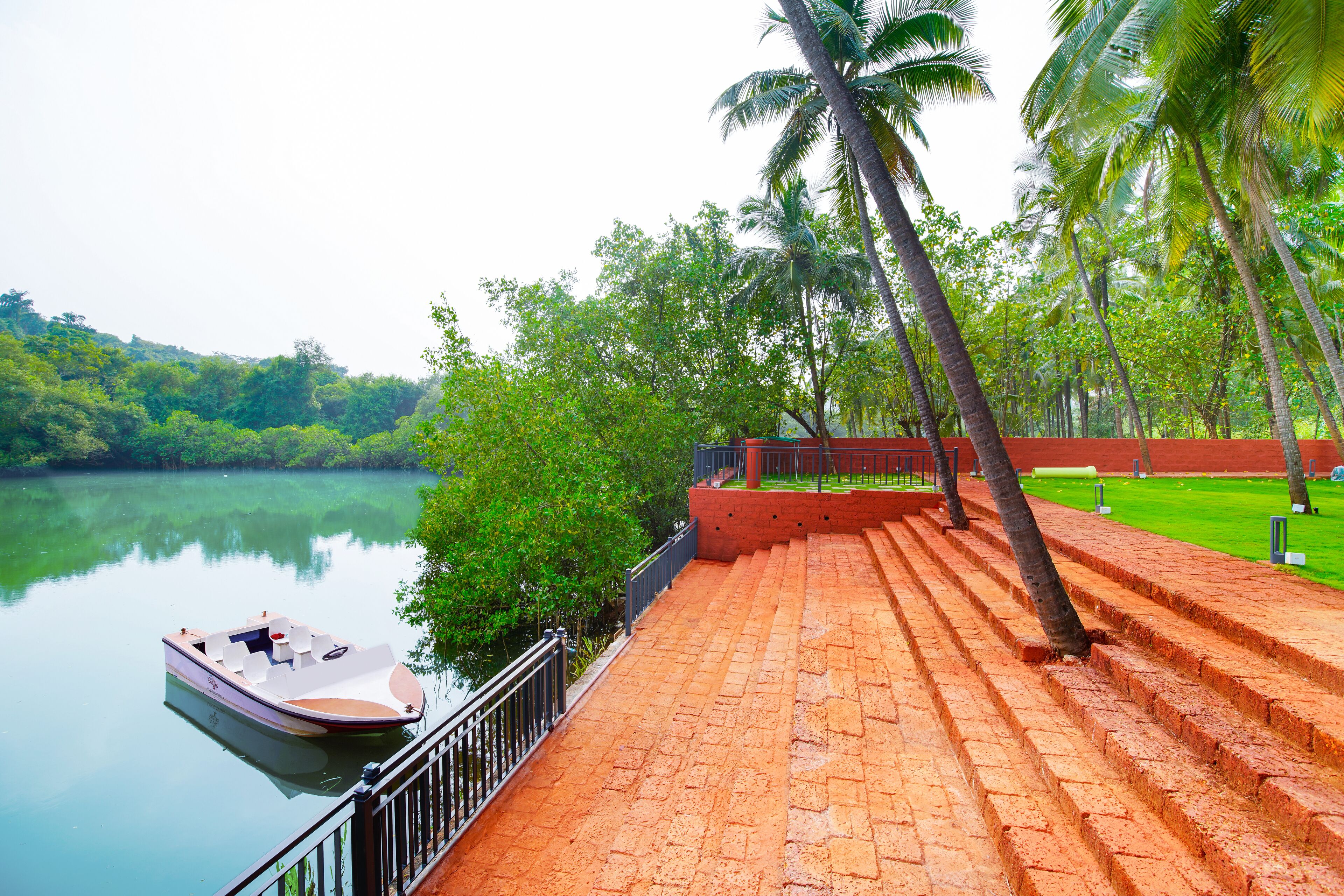 A boat docked at a calm river with a brick pathway leading to a grassy area with palm trees.