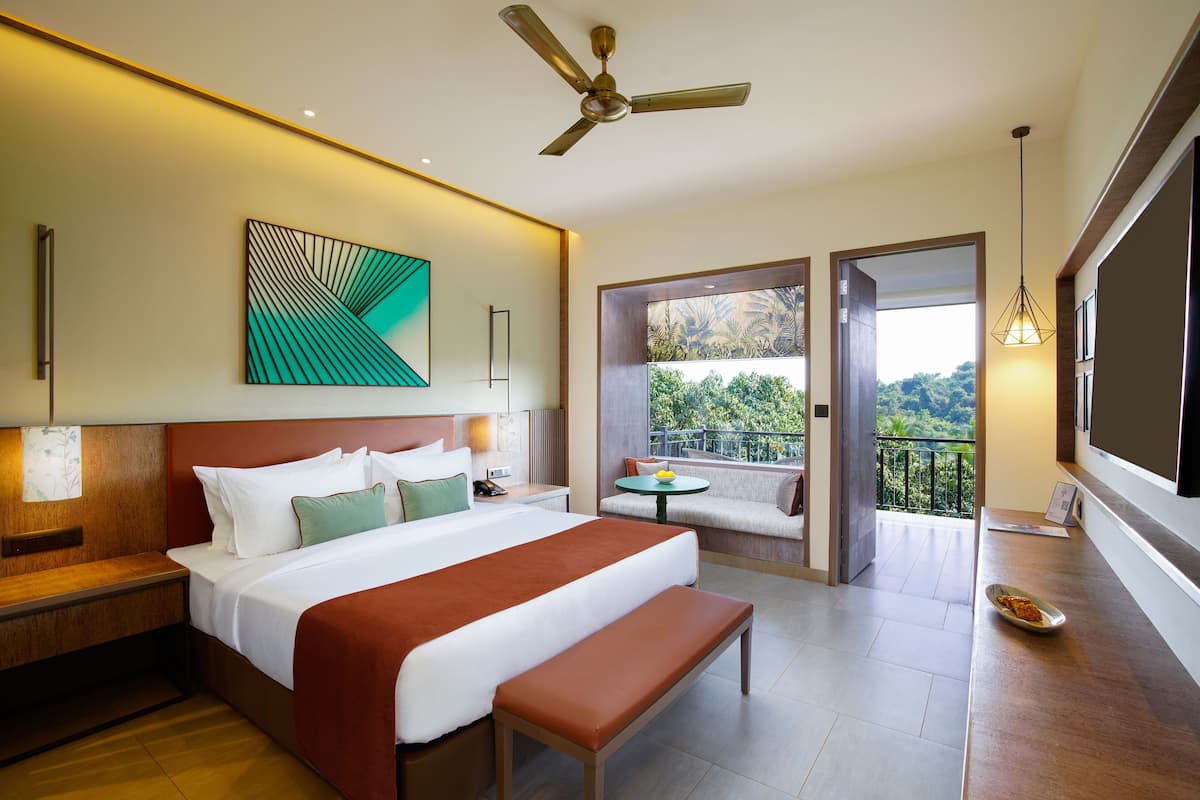 A hotel room with a large bed, a bench, a balcony with a view, and a ceiling fan.