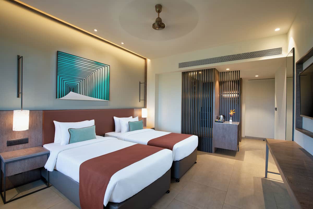 A modern hotel room with two beds, a desk, and a seating area.