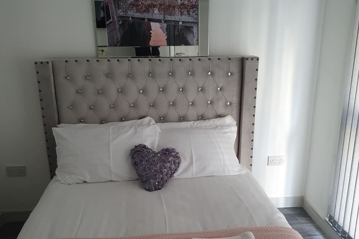 A neatly made bed with a heart-shaped pillow, a pink blanket, and two folded towels.