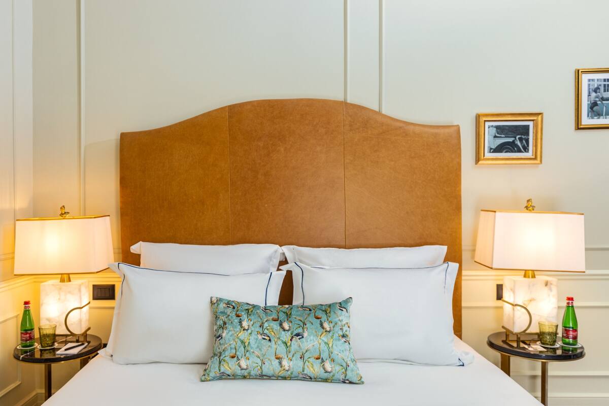A hotel room with a large bed, two bedside tables, two lamps, and a framed picture on the wall.