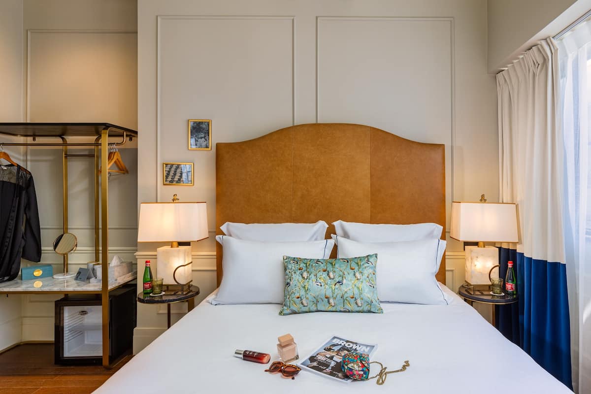 A hotel room with a large bed, two bedside tables, a wardrobe, and a window with curtains.