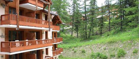 A multi-story wooden building with balconies, surrounded by a forested hillside.