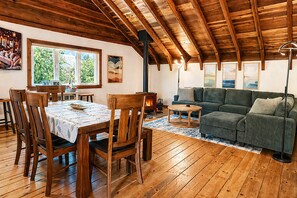 Uma sala de estar acolhedora com teto de madeira, lareira, sofá e um espaço de jantar com cadeiras e mesa.