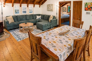 A cozy living room with a sectional sofa, a wooden coffee table, and a dining table with chairs.