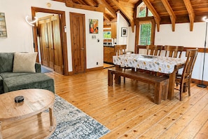 Uma sala de estar com piso de madeira, um sofá, uma mesa de jantar com cadeiras e um banco.