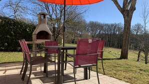 Eine Terrasse mit einem Steinofen, roten Stühlen und einem Tisch unter einem orangefarbenen Sonnenschirm.