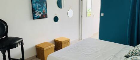 A bedroom with a bed, a chair, a small table, and a painting on the wall.