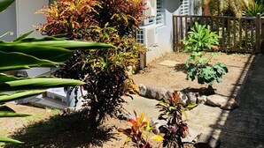 A two-story building with a white exterior, surrounded by various plants and a wooden fence. - Villa Fresh&Cosy Trois-Ilets, Swimming Pool, Sea View, 3***, France (Les Trois-Ilets)