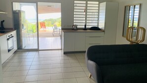 A modern kitchen with white cabinets, a black sofa, and a view of a balcony with chairs. - Villa Fresh&Cosy Trois-Ilets, Swimming Pool, Sea View, 3***, France (Les Trois-Ilets)