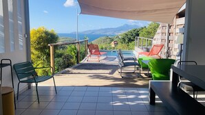 A balcony with a pool, chairs, and a view of mountains. - Villa Fresh&Cosy Trois-Ilets, Swimming Pool, Sea View, 3***, France (Les Trois-Ilets)