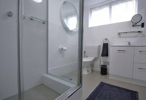 A modern bathroom with a glass shower enclosure, a toilet, a sink with a mirror, and a window providing natural light.