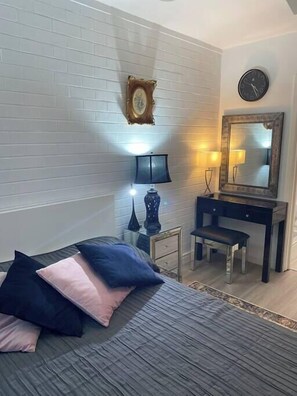 A bedroom with a bed, bedside tables, a desk, a mirror, and a clock on the wall.