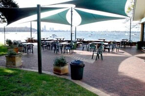Une terrasse extérieure avec des tables et des chaises, une poubelle et une vue sur l’eau, avec des bateaux.