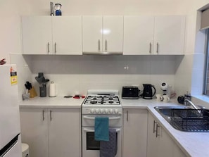 Une cuisine avec des meubles blancs, une cuisinière à gaz, un four à micro-ondes, un grille-pain et un évier.