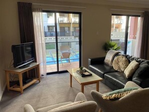 A living room with a television on a stand, a sofa, a coffee table, and a sliding glass door leading to a balcony.