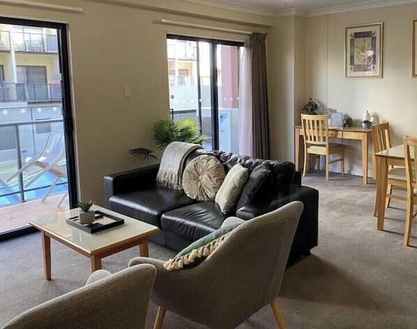 A living room with a sofa, a coffee table, a dining table with chairs, and a balcony with chairs.