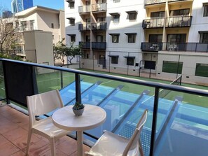 A balcony with a table and chairs, overlooking a tennis court and adjacent buildings.