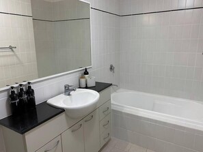 A bathroom with a white sink, black countertop, and a white bathtub. - Riverside City View Parking Netflix Wifi Wine FREE (Perth)