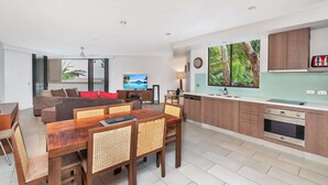 A modern living room with a sofa, TV, dining table, and kitchen area with cabinets and appliances.