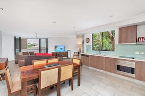 Enjoy a spacious living area with a sofa set and dining table, perfect for entertaining. The kitchen offers ample counter space and a view of the surrounding greenery.