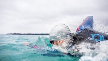 Un nageur portant un bonnet et une combinaison de plongée, partiellement immergé dans l’eau.